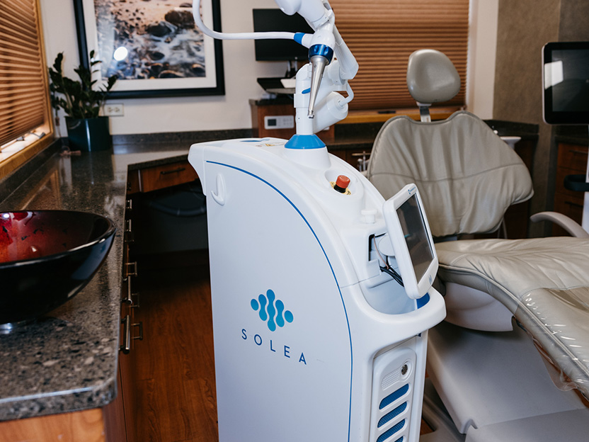 Dental laser device beside patient chair in modern clinic, illustrating advanced dental treatment technology.