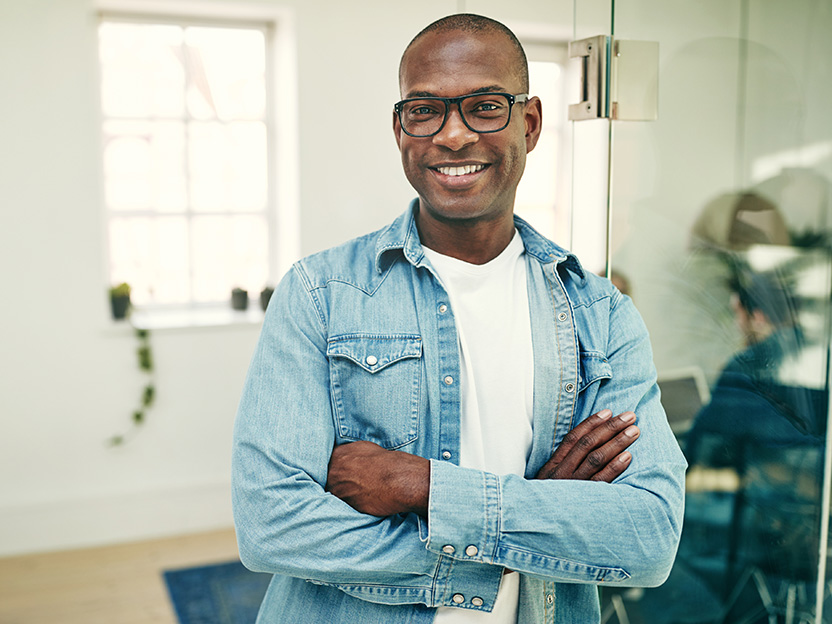 Smiling man with glasses and folded arms in a bright office, conveying confidence and approachability.