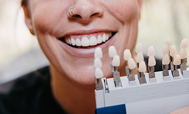 Smiling person holds tooth shade guide, illustrating selection of whitening or cosmetic dental results.