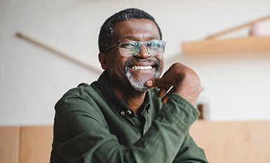 Smiling man with glasses resting chin on hand, conveying confidence and a friendly, approachable demeanor.