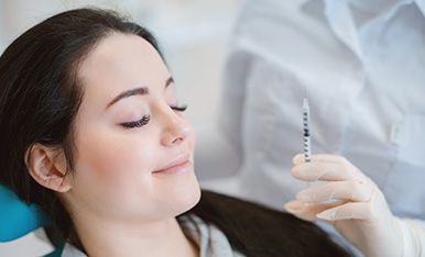 Patient smiles while holding a syringe, suggesting comfort and readiness for a cosmetic or dental injection.