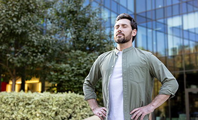 Man stands outdoors with hands on hips, eyes closed, suggesting confidence and well-being.