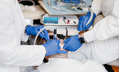 Close-up of dentists’ gloved hands using tools during a dental procedure on a patient.