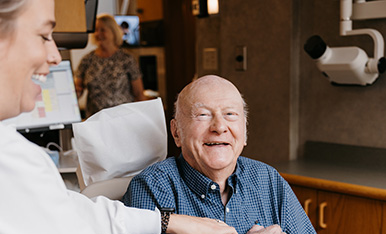 Extractions at Carlson Dental Group Smiling elderly patient sits in dental chair while clinician engages, conveying a friendly, comfortable visit.