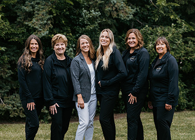 Team of six women standing outdoors, conveying a friendly, professional dental staff group in Stillwater, MN.