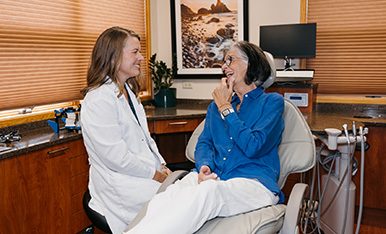 Dentist and patient smile and chat in exam chair, conveying comfort and positive experience.