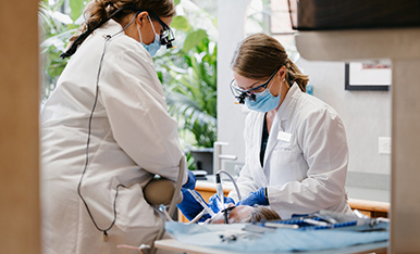 Periodontal therapy at Carlson Dental Group Dentists in masks and loupes perform a dental procedure together in a modern clinic.