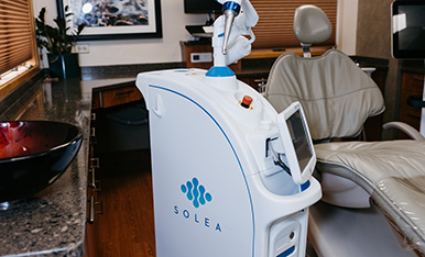 Dental laser device beside treatment chair in a modern clinic room.