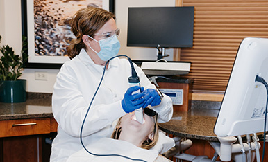 Dentist uses handheld tool on patient while viewing monitor, illustrating guided dental treatment.