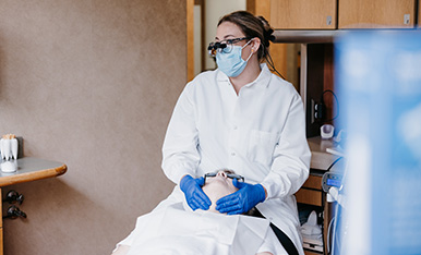 Dental professional wearing mask and loupes examining patient, indicating routine dental check or treatment