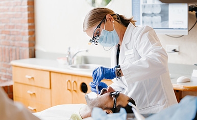 White filling done at Carlson Dental Group Dentist in mask and loupes performs a dental procedure on a patient in a clinic.