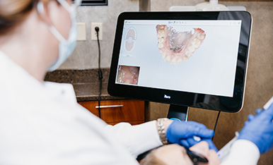 Dentist reviews digital 3D model of teeth on monitor during patient exam.